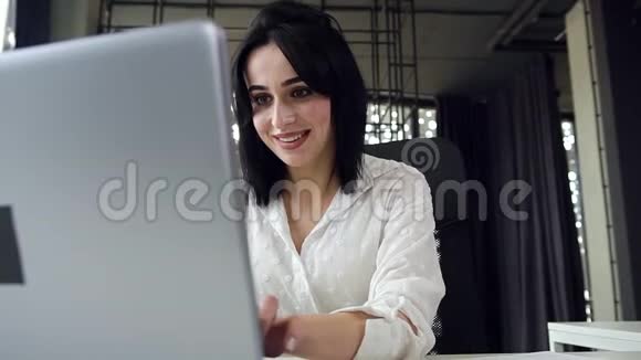 可爱的黑发年轻女商务小姐在笔记本电脑前工作在办公室里微笑着视频的预览图