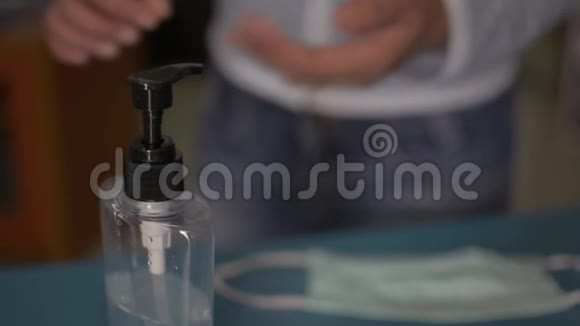 一名妇女在佩戴防护面罩前将洗手液滴入手中并对其进行消毒视频的预览图