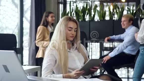 漂亮的金发年轻女商人在办公室工作场所了解平板电脑的信息视频的预览图