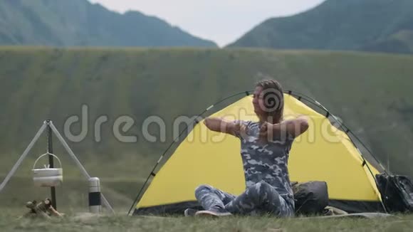 女游客睡后在晴朗的天气里双手挽起坐在山上的蜘蛛屋前视频的预览图