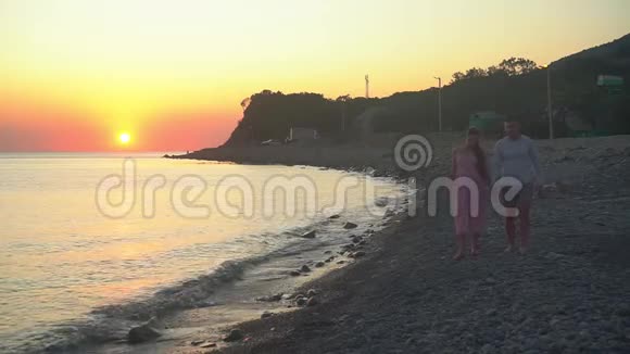 一对年轻的已婚夫妇正在散步一个男人和一个孕妇正在海滩上微笑着牵着手视频的预览图