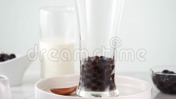 慢动作在玻璃杯中倒入奶茶在明亮的大理石桌子和白色托盘上有美味的台湾木薯珍珠泡视频的预览图