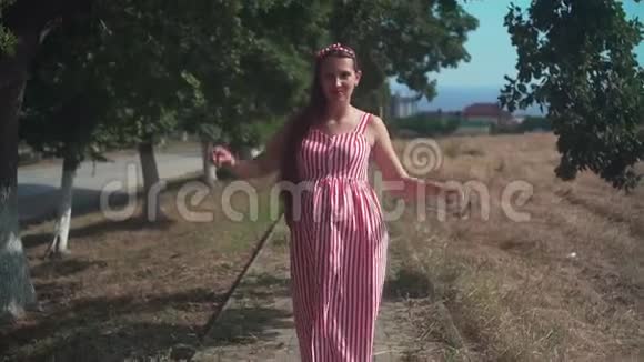 一个穿着红白条纹裙子的漂亮女孩怀孕了站在小路上开玩笑地跳舞视频的预览图
