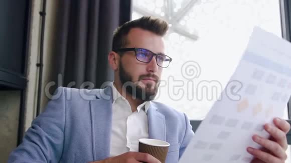 在阅读财务报告的同时办公室经理还在一边喝着纸杯里的咖啡视频的预览图