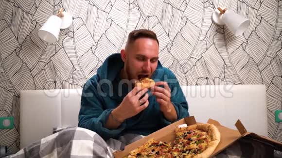大胡子穿绿色浴袍的男人在卧室的床上吃披萨享受慢节奏视频的预览图