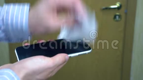 一个人小心地用湿抹把他的智能手机从细菌和病毒中消毒视频的预览图