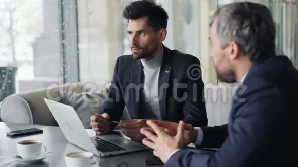 高管们在桌上的咖啡馆里谈论笔记本电脑讨论合同视频的预览图