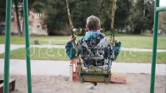 一个穿夹克的男孩在秋千上快乐地摆动为孩子们提供有趣的娱乐视频的预览图