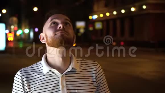 有胡子的帅哥抬起头然后在镜头里穿着条纹衬衫晚上站在街上视频的预览图