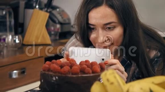 漂亮的黑发女孩为她的新鲜煮熟的覆盆子蛋糕制作照片和视频业余烹饪自制糕点和视频的预览图