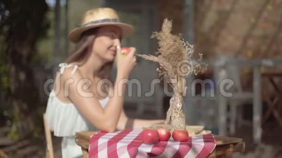 年轻的农村女孩戴着草帽穿着白色连衣裙坐在小桌前花瓶里插着装饰性的草嗅探着视频的预览图