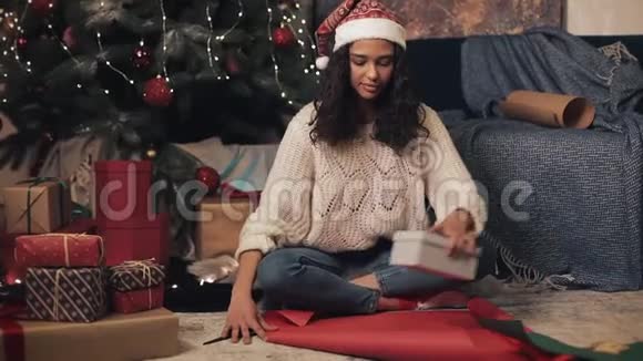 圣诞帽准备礼物的漂亮快乐女孩坐在圣诞树下年轻的布鲁内特女士视频的预览图