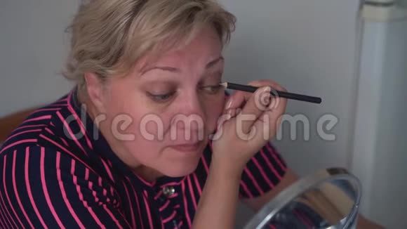 用铅笔把女人的脸合上做眼妆成年女性在镜子前用铅笔涂眼妆视频的预览图