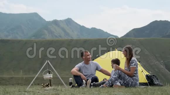 幸福的一家人带着一个孩子在帐篷附近的露营地笑着篝火视频的预览图