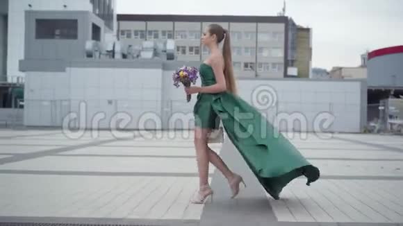 美丽的女孩穿着别致的裙子在清晨的城市背景上带着芬芳的野花漫步视频的预览图