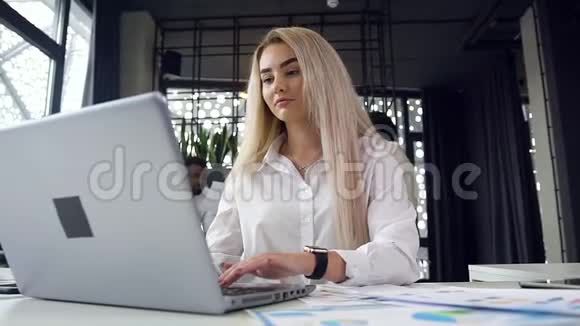一位迷人的勤劳的金发女商人拿着文件和电脑在工作场所工作视频的预览图