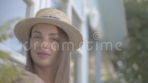 一位戴着草帽的漂亮年轻女人的特写脸看着镜头在户外快乐地微笑着情感乡村视频的预览图