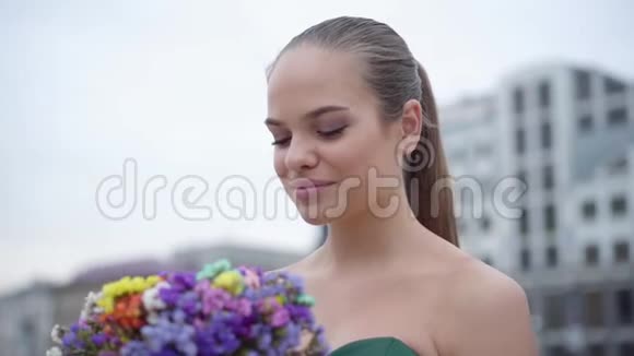 一个穿着别致裙子的可爱女孩在早晨的背景下闻到一束芬芳的野花的肖像视频的预览图