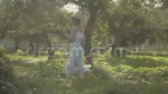 可爱的年轻女子戴着草帽穿着白色的长裙穿过绿色的夏日花园免费农村生活视频的预览图
