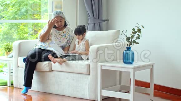 亚洲小孙女在沙发上和年长的女性一起看书视频的预览图