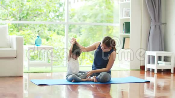 年轻的妈妈在家教可爱的女儿基本瑜伽视频的预览图
