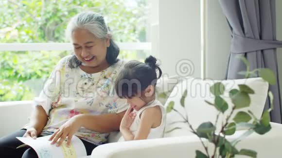 老妇人很高兴和可爱的孙女在沙发上聊天视频的预览图