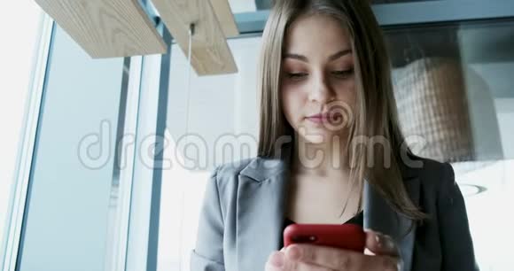 bif窗附近的办公室里一位年轻迷人的女士看着智能手机的画像视频的预览图
