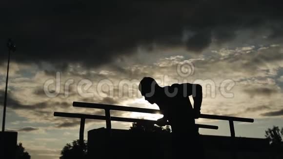 一个年轻人在户外双杠上做俯卧撑的剪影从底部看多云的天空没有阳光视频的预览图