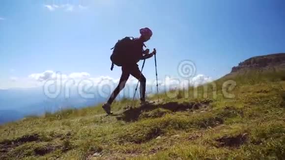 带着背包和徒步旅行杆的年轻女子走上山顶迎着蓝天慢动作夫人视频的预览图