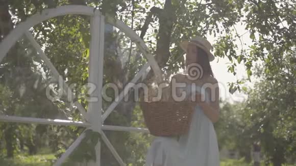 可爱的年轻女子戴着草帽手里拿着柳条篮子拿着草药看着镜头在绿色中微笑视频的预览图