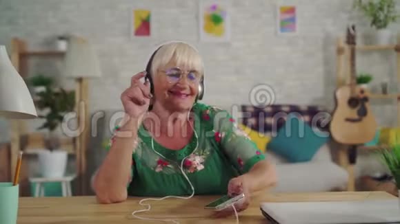 戴着耳机听音乐和跳舞的白发的快乐老妇人视频的预览图