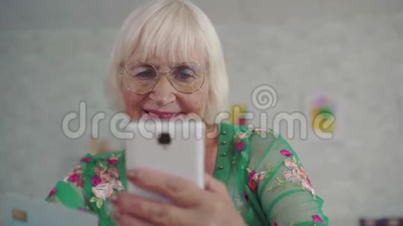 头发灰白的老年妇女持有银行卡使用智能手机视频的预览图