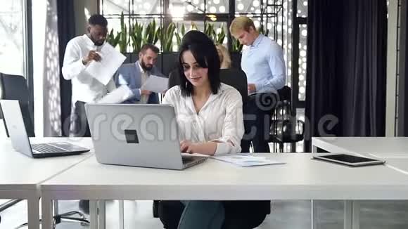 在公司背景下现代办公室里漂亮的黑发上班族在笔记本电脑上打字视频的预览图