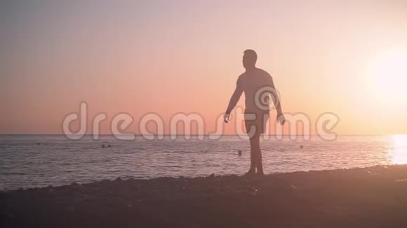 一个年轻人在日落的背景下沿着海岸散步一个人在日落的背景下沿着海滩散步视频的预览图