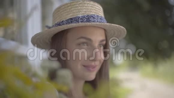 一位戴着草帽的可爱年轻女子的特写脸微笑着看着户外情感乡村生活方式自然美视频的预览图