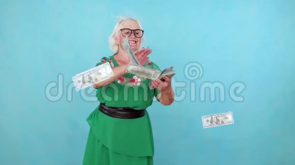 快乐积极的老妇人在蓝色背景上扔纸钞票视频的预览图