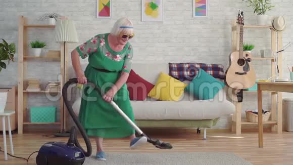 一位快乐的老年妇女戴着灰色头发的养老老人戴着眼镜像吉他一样弹奏着吸尘器视频的预览图