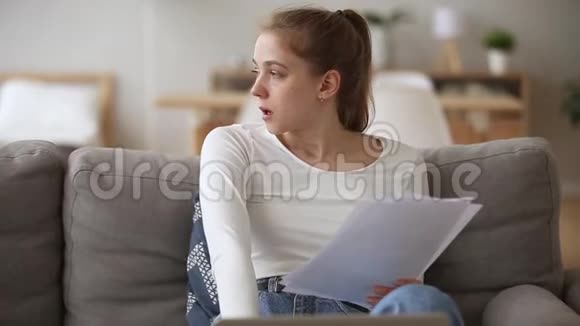 年轻女子坐在沙发上拿着文件感到沮丧视频的预览图