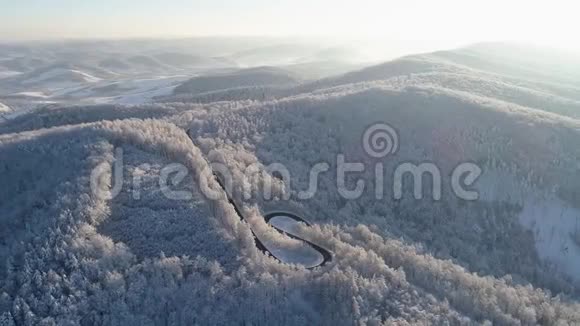 无人机拍摄的冬山景观与黑色蜿蜒的道路之间的雪树视频的预览图