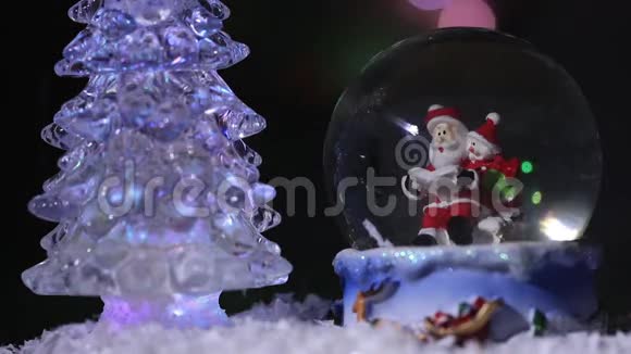 圣诞老人靠近一棵美丽五颜六色的新年杉树坐在玻璃球里为孩子们准备新年礼物视频的预览图