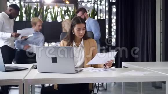 漂亮有经验的年轻女性办公室工作人员在现代工作场所比较报告和计算机数据视频的预览图