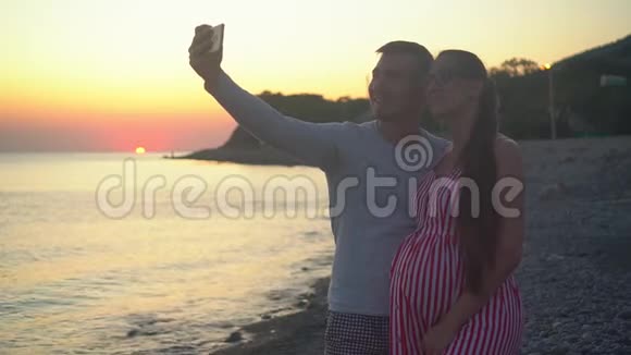 一对年轻的夫妇站在海上日落的背景上一男一女正在自拍视频的预览图