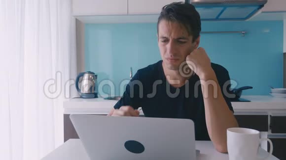 沮丧的年轻人在厨房里用笔记本电脑工作时感到痛苦和头痛视频的预览图