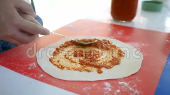 快乐的孩子们在厨房准备自制披萨小女孩正在用勺子涂抹番茄酱和面粉揉成的披萨家庭娱乐视频的预览图