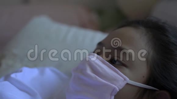 母亲的手轻轻地摸着女儿的额头亚洲可爱的女孩戴着防护面具生病时躺在床上视频的预览图