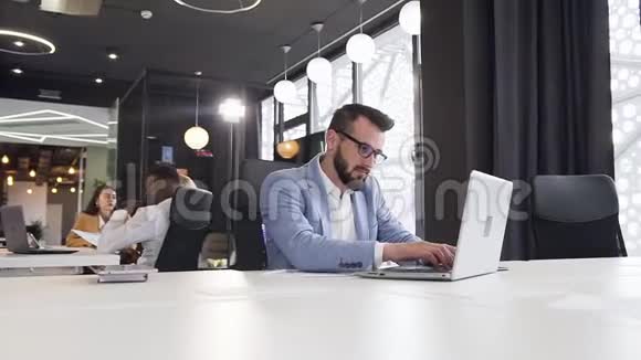 有目的的英俊上班族使用他的电脑不同的财务报告并在后台打电话视频的预览图