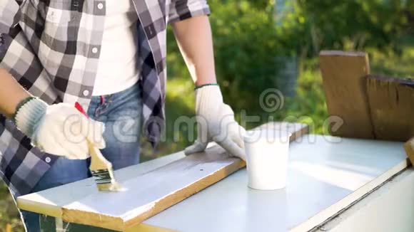 在阳光明媚的后院女人的双手用白色油漆在木板上作画视频的预览图