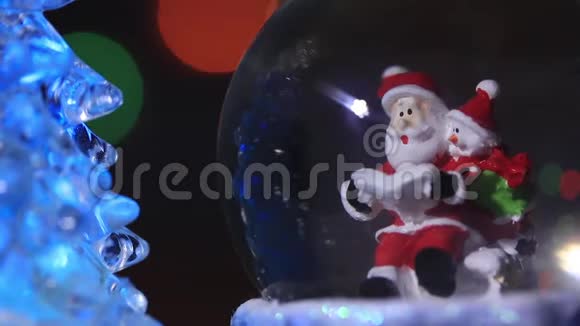 圣诞老人靠近一棵美丽五颜六色的新年杉树坐在玻璃球里为孩子们准备新年礼物视频的预览图