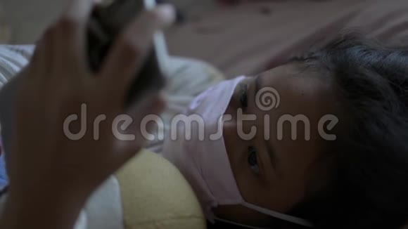 亚洲可爱的女孩戴着防护面具躺在床上时使用手机电晕病毒防护视频的预览图