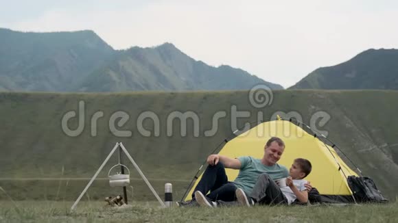 快乐的父子一起放松在群山的背景下在帐篷前欢乐视频的预览图
